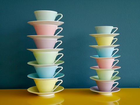 Stack of colorful vintage tea and coffee cups on yellow table against petrol background.