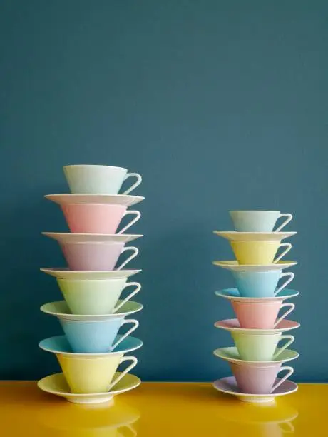 Photo of Stack of colorful vintage tea and coffee cups on yellow table against petrol background.