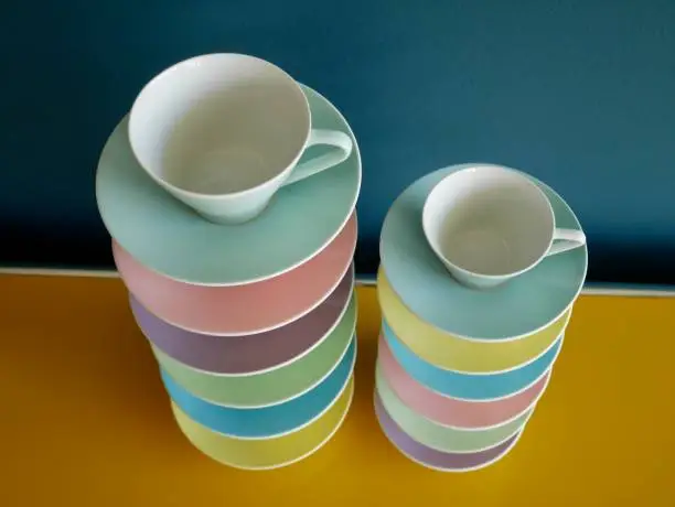 Photo of Aerial view of colorful stacked vintage tea and coffee cups on yellow table against petrol background.
