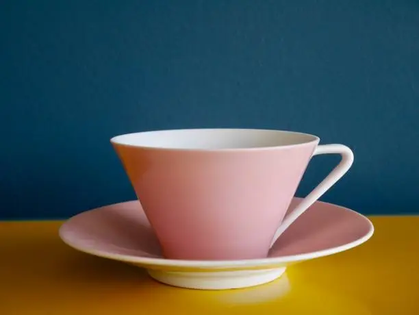 Photo of Vintage pastel tea cup on yellow table against petrol background. Afternoon tea party.