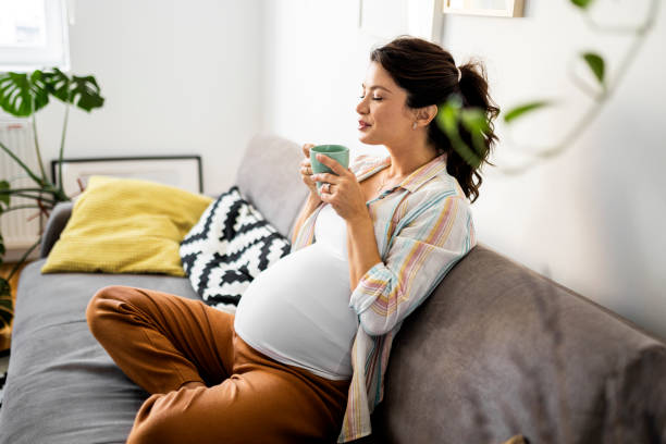 Pregnant woman resting on sofa drinking coffee stock photo