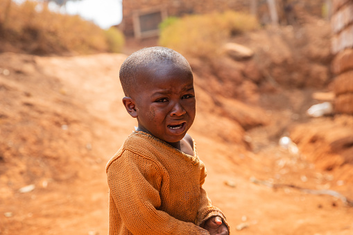 Portrait of a poor African child crying in the village, he wears dirty clothes