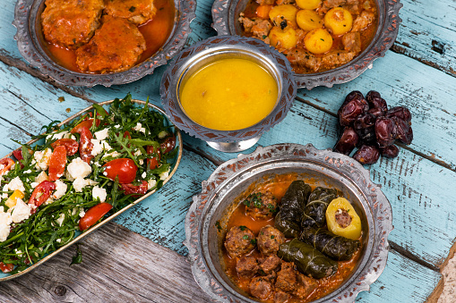 Eid Mubarak Traditional Ramadan Iftar dinner. Assorted tasty food in authentic rustic dishes on wooden blue background. Turkish Bosnian food meat kebab, pita, Sarma, klepe, sogan dolma. High quality