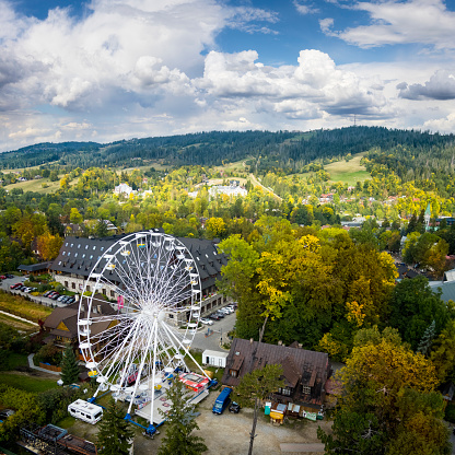 A booth on a Ferris wheel against a clear blue sky and trees in the park. Lightpost is in the foreground.