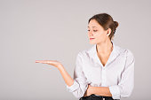 A businesswoman presents a product in the palm of her hand with a copy space for advertising on a gray background.