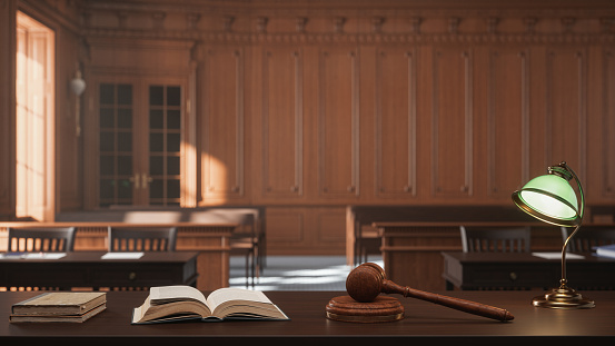 Interior of an empty courtroom with gavel, law books and sounding block on the judge's desk.