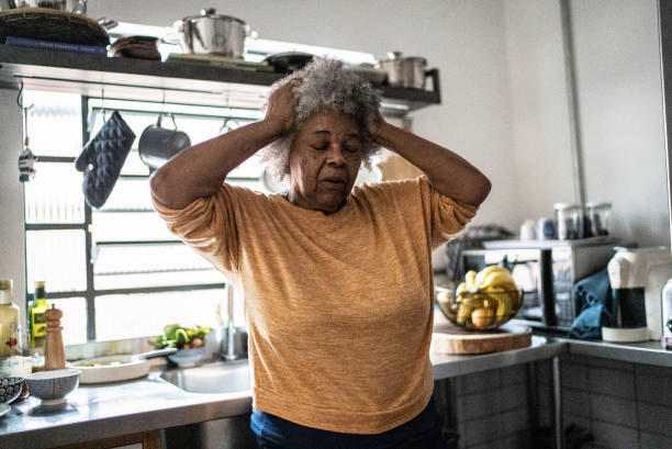 worried senior woman in the kitchen at home - female emotional stress african ethnicity loss imagens e fotografias de stock