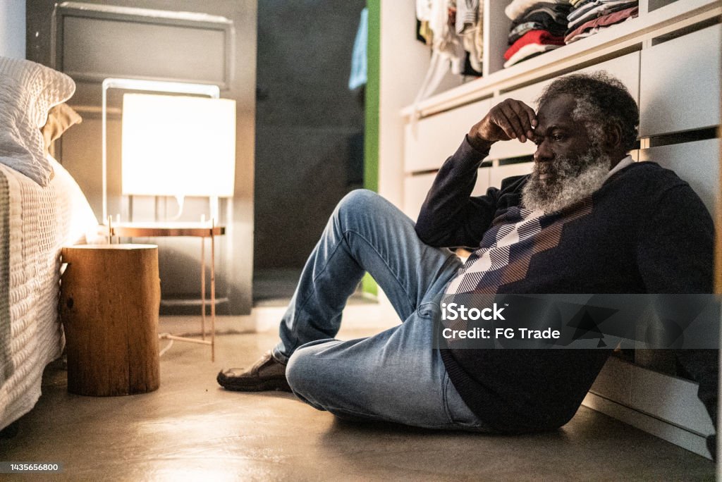 Sad senior man sitting on floor of the bedroom at home Senior Adult Stock Photo