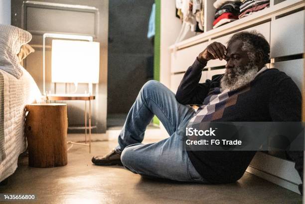 Sad Senior Man Sitting On Floor Of The Bedroom At Home Stock Photo - Download Image Now