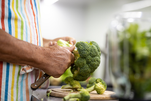 Senior man preparing broccoli, cutting broccoli at home kitchen, preparing a healthy dish full of nutrients.