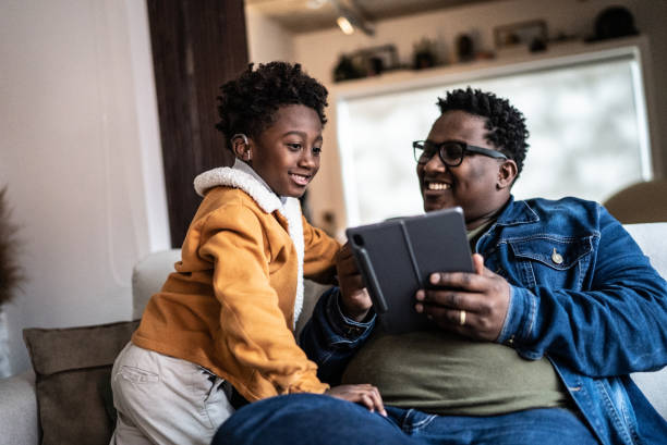 Father showing something on digital tablet to his son at home Father showing something on digital tablet to his son at home deaf stock pictures, royalty-free photos & images