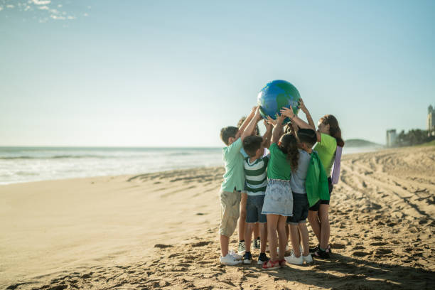 дети держат планету на пляже - sustainable resources environment education cleaning стоковые фото и изображения