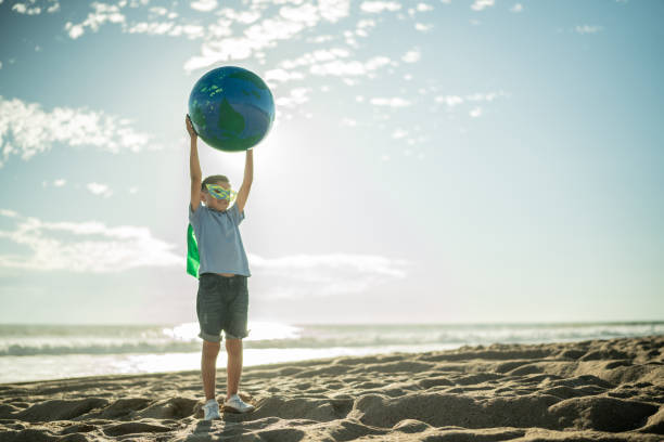 superheroe boy holding an earth sphere at the beach - sustainable resources environment education cleaning imagens e fotografias de stock