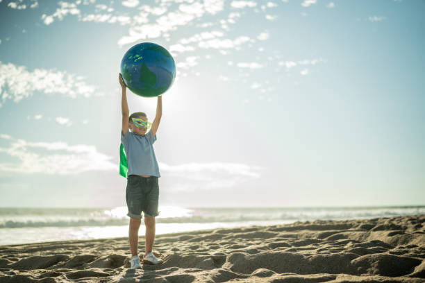 мальчик-супергерой держит земную сферу на пляже - sustainable resources environment education cleaning стоковые фото и изображения