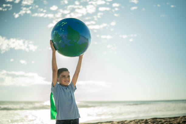 Superheroe boy holding an earth sphere at the beach