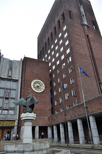Oslo, Norway - Brick town hall building with golden clock, statue and flags