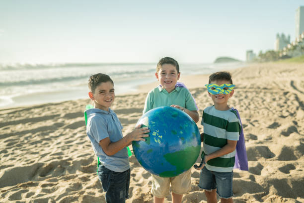 retrato de meninos super-heróis com uma esfera de terra na praia - recycling green environment superhero - fotografias e filmes do acervo