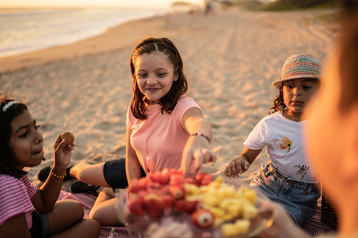 Girls taking a strawberry at a picnic at sunset on the beach