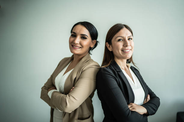 retrato de dos empresarias con los brazos cruzados sobre fondo gris - two people back to back businesswoman women fotografías e imágenes de stock