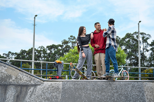 Group of Latin American skateboarder friends, chatting while laughing and enjoying together at a skatepark.