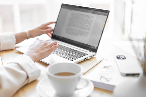 Primer plano de la mano femenina derecha. Una mujer irreconocible está escribiendo texto en una computadora portátil. Taza de café, teléfono inteligente, vasos en el escritorio. Primer plano borroso. photo
