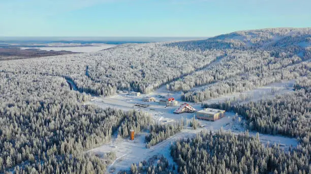 Photo of Top view of ski resort at foot of mountain. Footage. Secluded ski resort at foot of hill with ski slopes is popular in winter season. Clear sunny day on ski slopes of winter resort