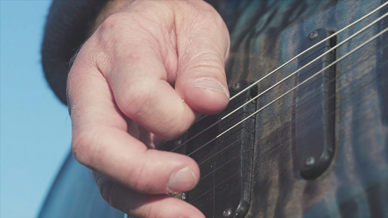 Close-up of hands playing bass guitar. Stock. Male hands of guitarist playing chords on bass guitar. Music performed on guitar.