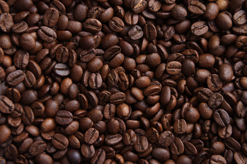 Fresh dark brown coffee beans on white table. Pattern background. Closeup. Top down view.