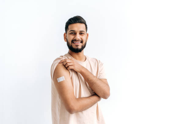 istock Indian happy guy stands on isolated white background with a plaster on his shoulder, received a vaccine against various diseases, looks at the camera, smiles. Healthcare and immunity concept 1435687140