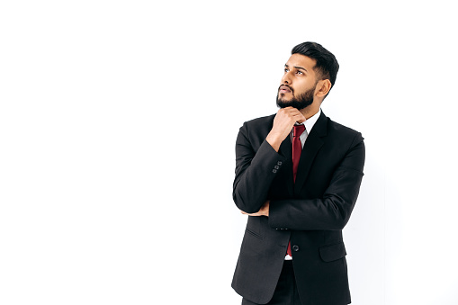Puzzled thoughtful elegant influential arabian or indian man in formal suit, stand on isolated white background, pensively looking away, thinking, planning, dreaming. Copy-space for your presentation