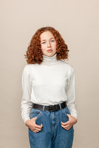 Studio portrait of a red-haired teenage girl in a white sweater on a beige background
