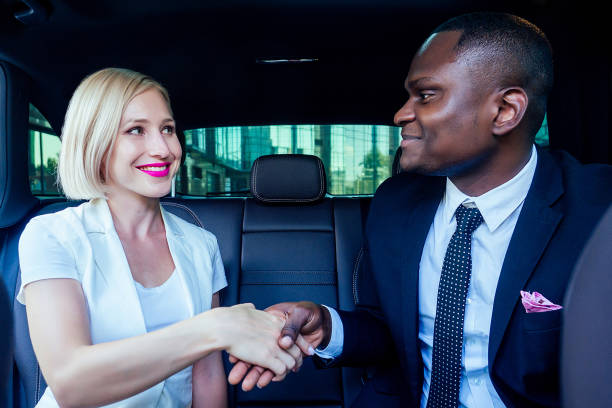 donna d'affari bionda di successo imprenditrice datore di lavoro con trucco in vestito bianco con un bel capo afro-americano uomo industriale in nero elegante vestito giacca stretta di mano che lavora in auto buon affare - industrialist foto e immagini stock