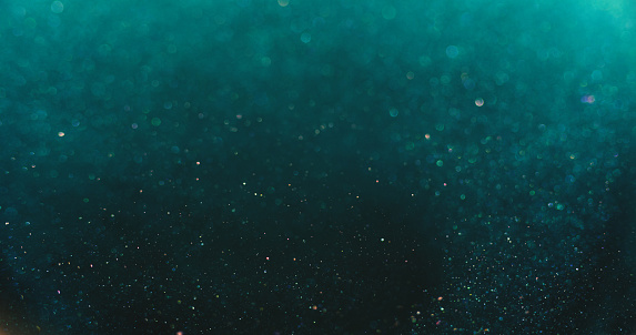 Bokeh light overlay. Blur glitter texture. Shimmering water bubbles. Defocused verdigris green blue orange color particles on dark abstract background.