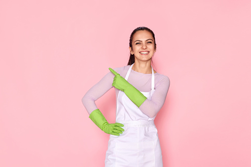 beautiful caucasian woman in rubber gloves pointing fingers aside at copy space on pink background. cleaning