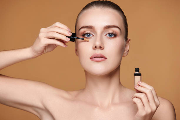 woman applying concealer under her eyes on beige background portrait of beautiful woman applying concealer under her eyes on beige background vogue cover stock pictures, royalty-free photos & images