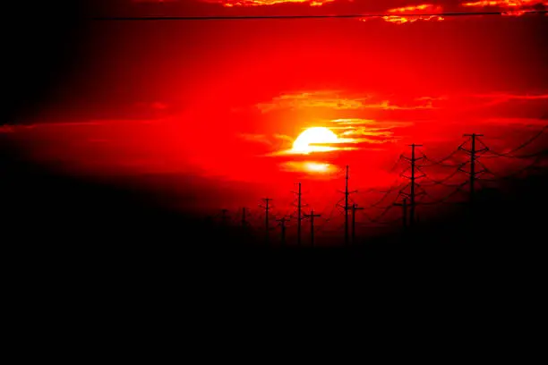 An other-worldly, blood-red sun setting behind power lines and power poles in Mountain Home, Idaho, USA.