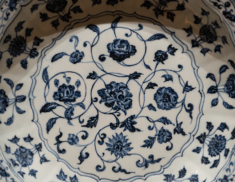 A blue and white Asian-style pottery teapot with a circular opening is in the forefront.  A softly blurred blue English Fine Bone China teacup can be seen through the circular design.