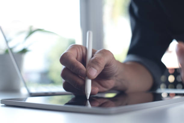 istock Close up of man hand using stylus pen on digital tablet screen with laptop computer on office table with blurred background, business and technology concept 1435723457