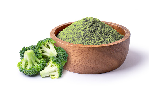 Fresh Broccoli and green herbal powder in wooden bowl isolated on white background.