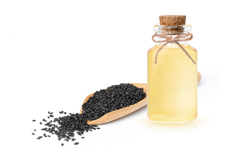 Sesame oil in glass bottle with black sesame seeds in wooden scoop isolated on white background.