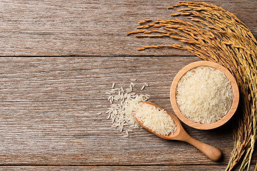 White rice, natural long rice grains (Thai jasmine rice) and paddy rice in wooden bowl isolated on wooden table background. Top view. flat lay. Copy space.