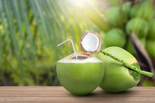 Coconut juice (coconut water) and fresh young green coconut with coco nut tree blurred background.