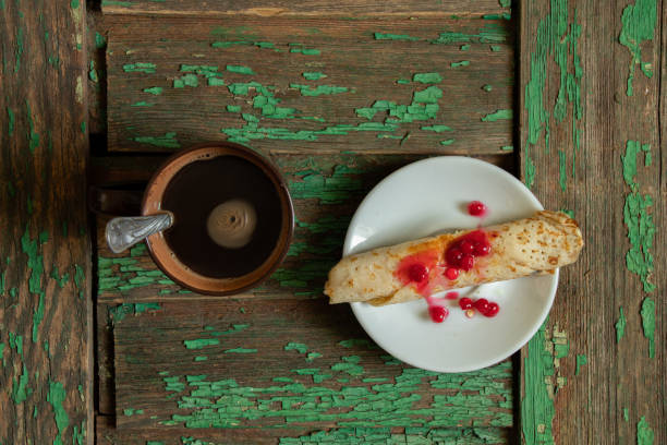 rolled pancake with viburnum and sugar on a teatka next to a cup of coffee on an old wooden table, morning coffee with a dissert rolled pancake with viburnum and sugar on a teatka next to a cup of coffee on an old wooden table, morning coffee with a dissert on the table dissert stock pictures, royalty-free photos & images