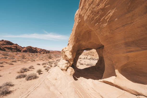 Overton, Nevada, USA - February 25, 2010: Valley of Fire. Landscape with flat red rock with holes on top of lined and broken rock parts under light blue sky with dry desert floor in front.