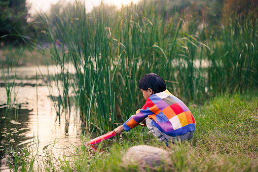 Asian boy playing with water by the pond