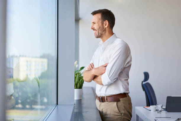 istock Smiling businessman looking through window at office 1435745669
