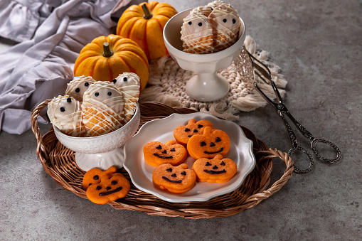 Plate of Halloween Jack o Lantern cookies and mummy vanilla madeleines.