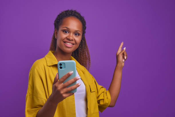 istock Young joyful African American woman with phone points finger at copy space 1435758328