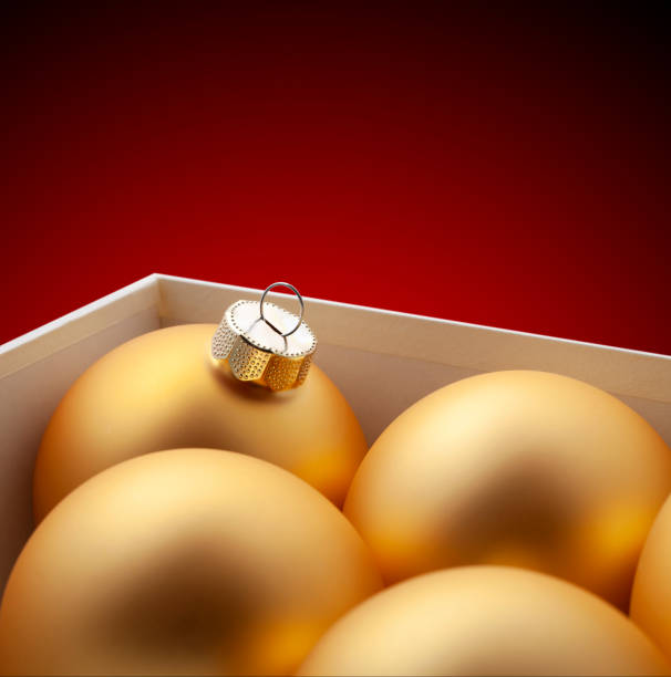 Box of golden Christmas balls on red background.