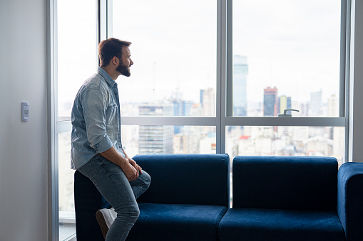 Mid-shot portrait of young businessman looking out the window at city skyline